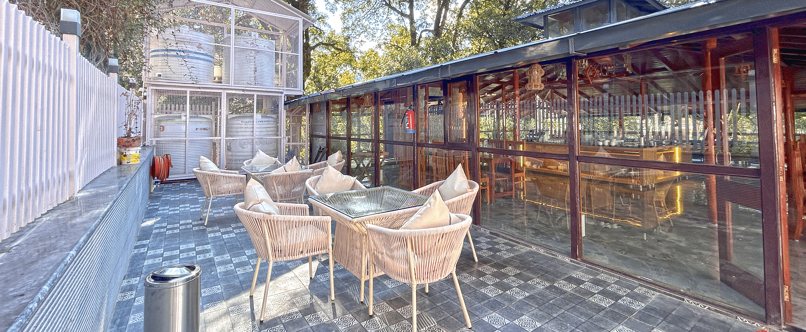 The exterior image of the restaurant featuring chairs and tables with the background of a clear sky and trees - DLS The Emerald, Nainital