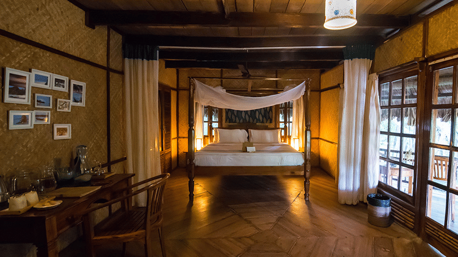 One of the Fan Cooled Duplex Cottages at Barefoot at Havelock featuring a plush bed with a canopy and a desk facing the wall with photos of beaches on it