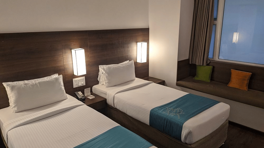 The Comfort Room at Temple Tree Hotel, Bangalore showcasing twin beds, a wooden head board, overhead lamps, and a large glass window.