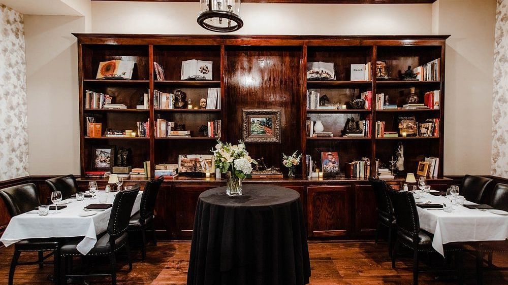 A  library with bookshelves, elegant seating, and a round table in the center, creating a sophisticated reading space.- The Grand Hotel & Ballroom, McKinney