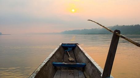 Wooden boat on a calm lake at sunset, with warm golden hues reflecting on the water and hills in the distance.