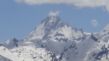 Snow-covered mountain peak with rugged slopes and partly cloudy sky, representing a winter alpine scene.