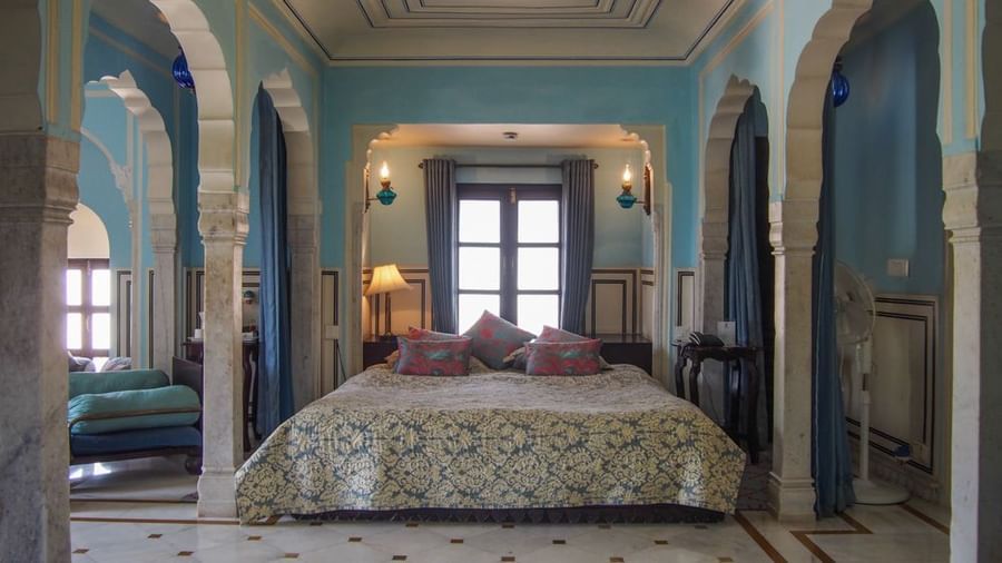 A bedroom at Royal Heritage Haveli featuring a large bed with a patterned cover, blue walls, and arched architectural details.