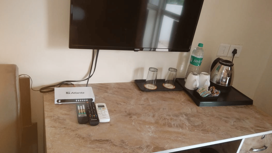 A desk with a wall-mounted TV, water bottle, and remote at Livbox, Rudrapur.