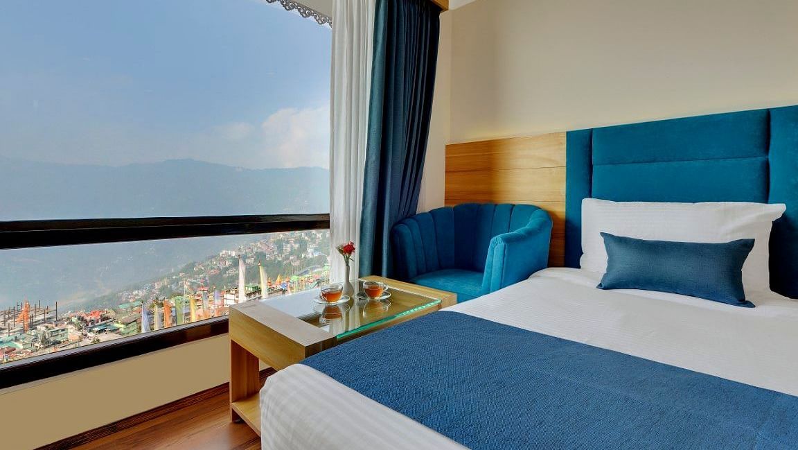 An image of the premium executive room with a bed, a table, a chair and an expansive window overlooking the view - Yashshree Sikkim Blossom, Gangtok