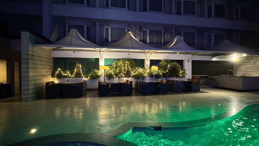 A nighttime view of an outdoor lounge area with canopy umbrellas, plants, and a glow-in-the-dark green swimming pool - Cenneys Gateway