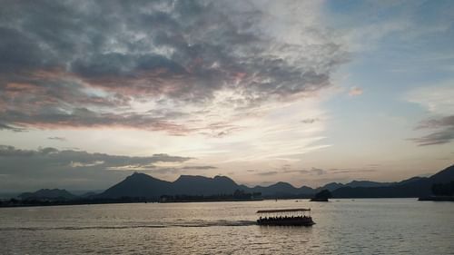 Boat sailing on a lake with mountain backdrop during sunset in Udaipur, near Golden Tulip.