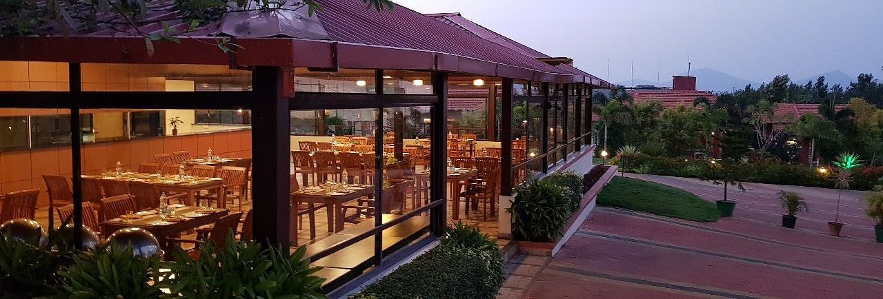 View from outdoor area of a restaurant in a wooden structure and lush greenery | Sheesham Restaurant | Woodstock Resorts, Coorg