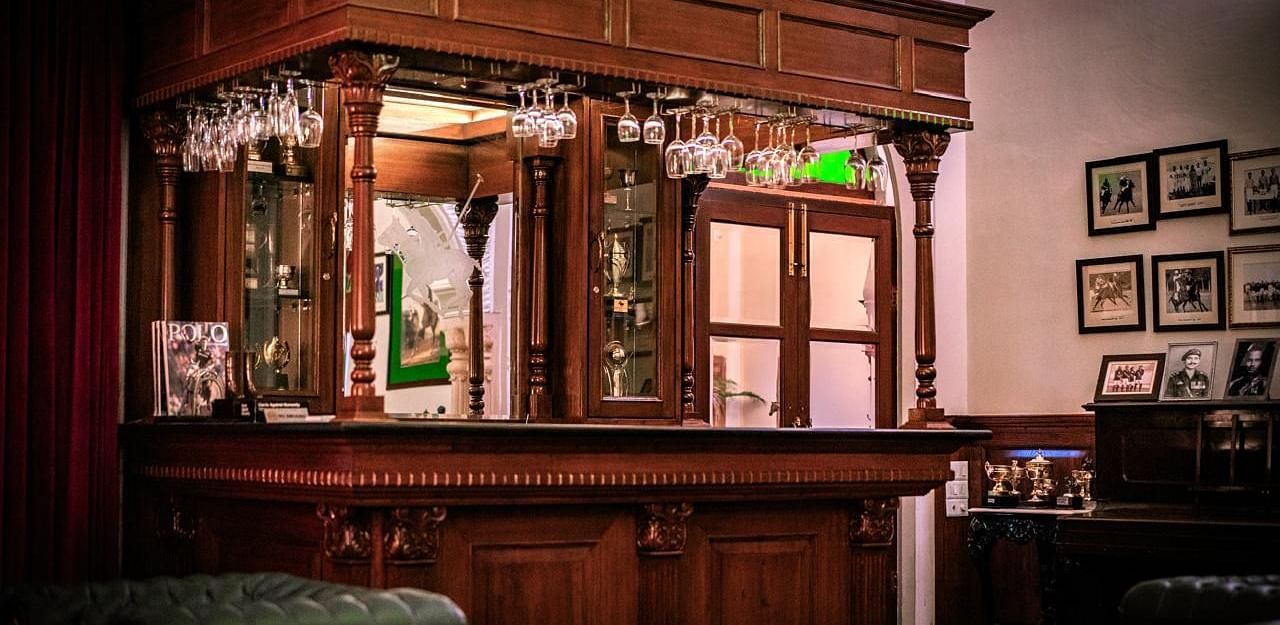 A classic, ornate wooden bar with hanging glassware and framed pictures on the wall - Khas Bagh, Jaipur