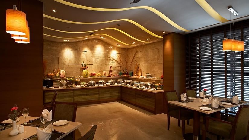 An image of a restaurant featuring several sets of tables and chairs at each corner and there are ceiling lights as well as lamps lighting up the area at Adarsh Hamilton