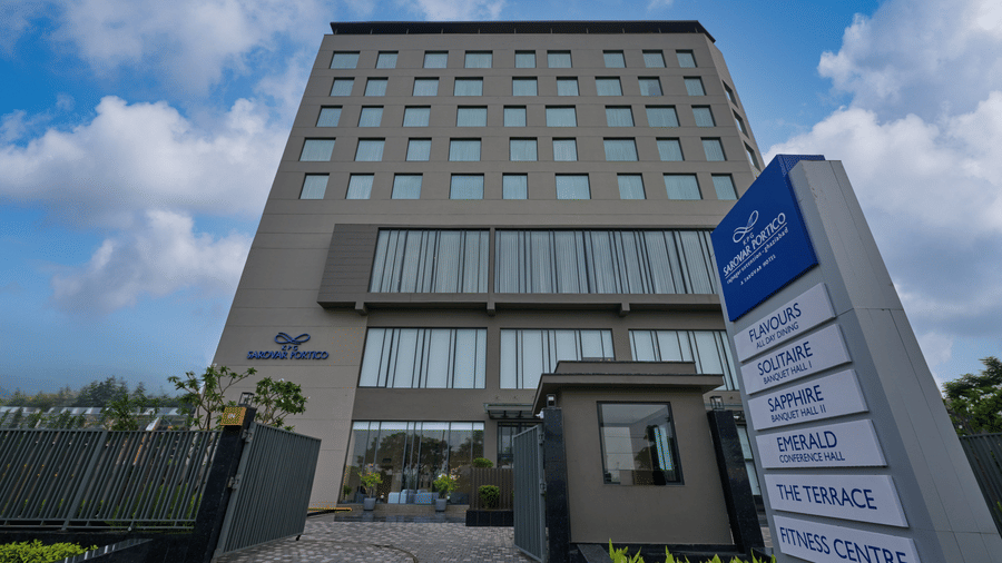 A hotel building front at KPG Sarovar Portico, Raj Nagar Extension, Ghaziabad featuring a multi-storey facade, entry gate, boundary fence, and a signage board.