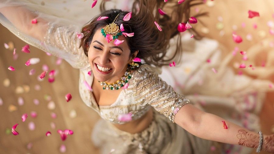 A woman in her wedding attire dancing while the flower petals are falling on her from above.