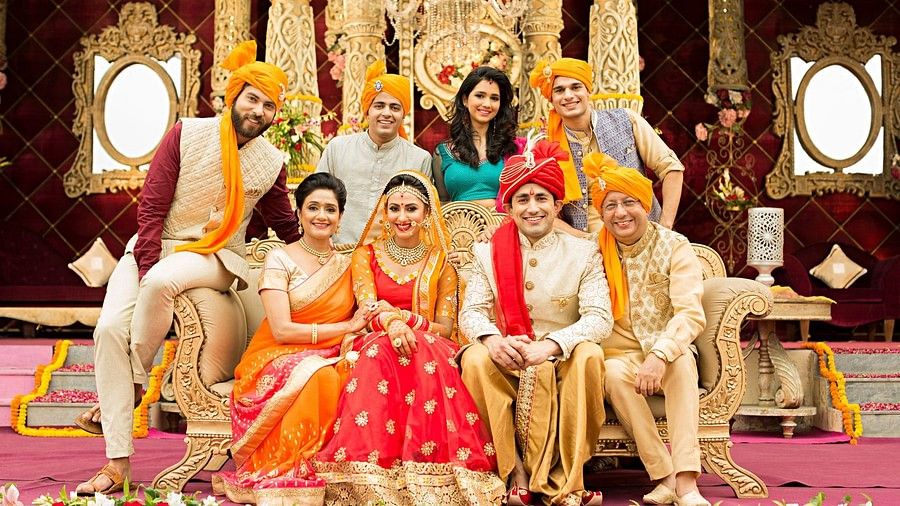 Indian family sitting together in front of a huge chair and posing for the camera in a wedding.