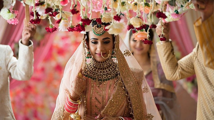 Indian bride walking down the aisle with four brother around her. The brother are holding a decorated small flower blanket above her head.