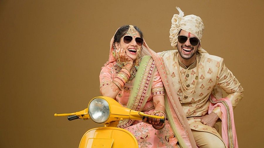 Bride and groom in ethic wear, sitting in a scooter and posing for the photoshoot.