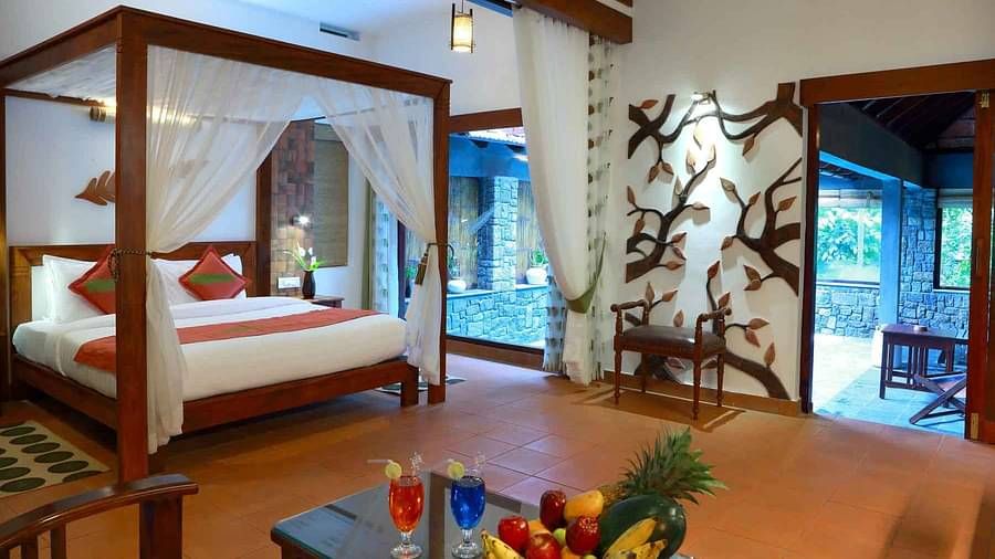 A four-poster bed in a room with wooden decor and furniture | Vythiri Resort. Wayanad