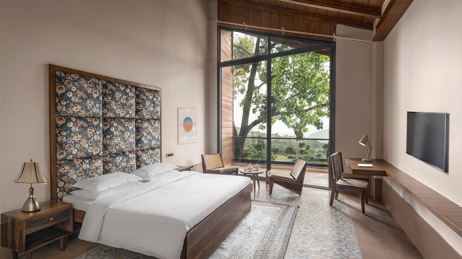 A warmly decorated room featuring a window with nature views, patterned fabric on the wall behind the bed, and a cosy sitting area - The Samai, Bhimtal