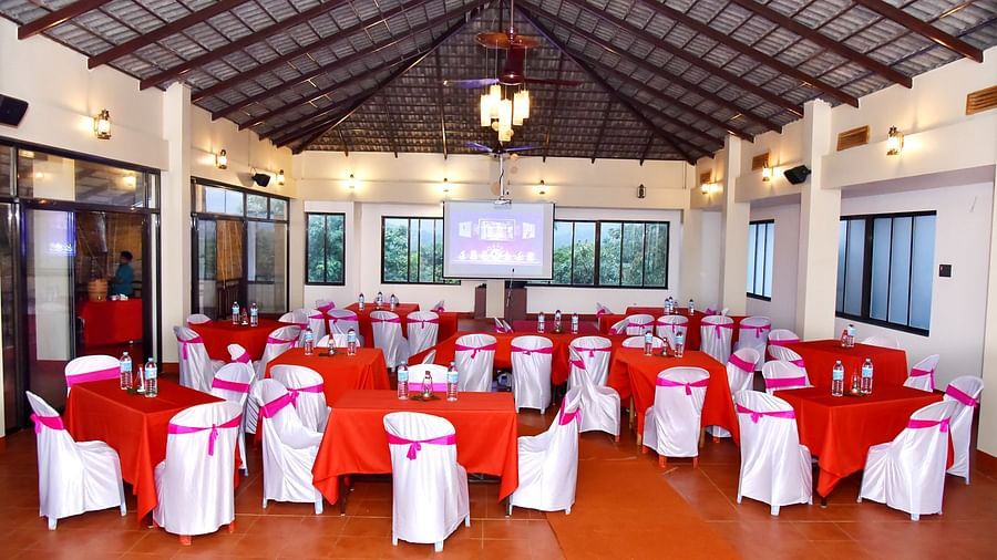 A banquet hall at Forest Escapes Koyna is elegantly set up with draped chairs and round tables, possibly for an event.