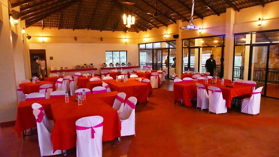 A banquet hall at Forest Escapes Koyna is prepared for a gathering with red tablecloths and white chair covers.