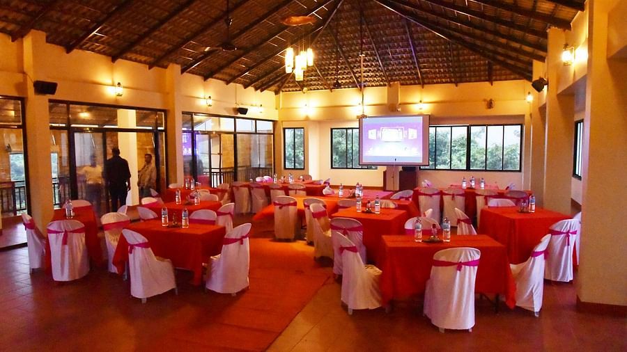 The spacious event hall at Forest Escapes Koyna is filled with round tables draped in red, prepared for a gathering.