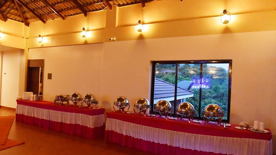 The well-lit event space at Forest Escapes Koyna is arranged with tables and chairs, ready for guests.