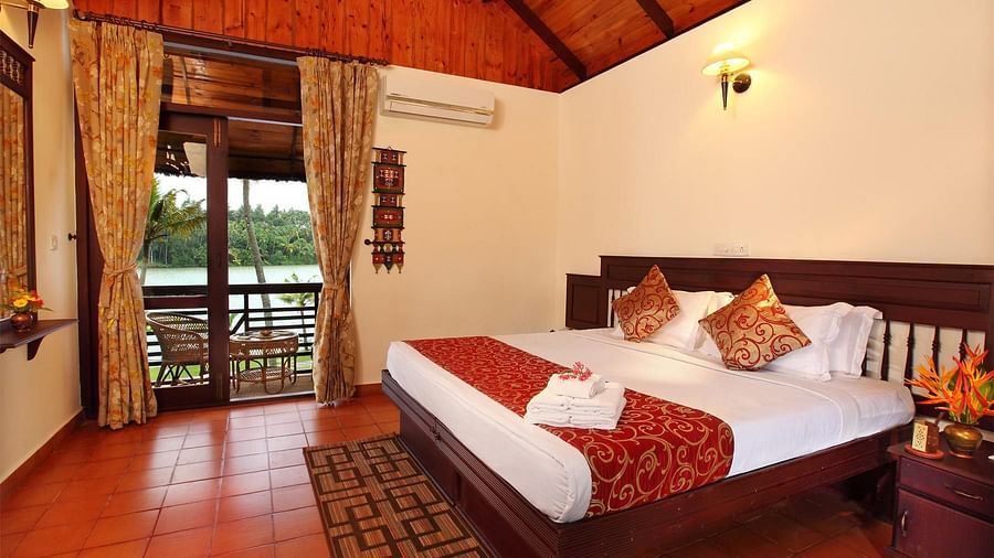 Spacious bed with neatly arranged cushions, complemented by a balcony with two pathways and a sofa arranged nearby to enjoy the view