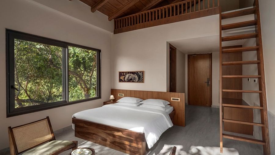 A minimalist bedroom featuring a large window with a forest view, wooden furniture, and a loft area - The Samai, Bhimtal