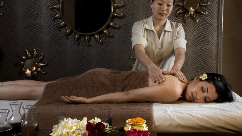 A guest lying on a spa bed receiving a massage from a therapist at Heritage Village Resorts & Spa, Manesar.