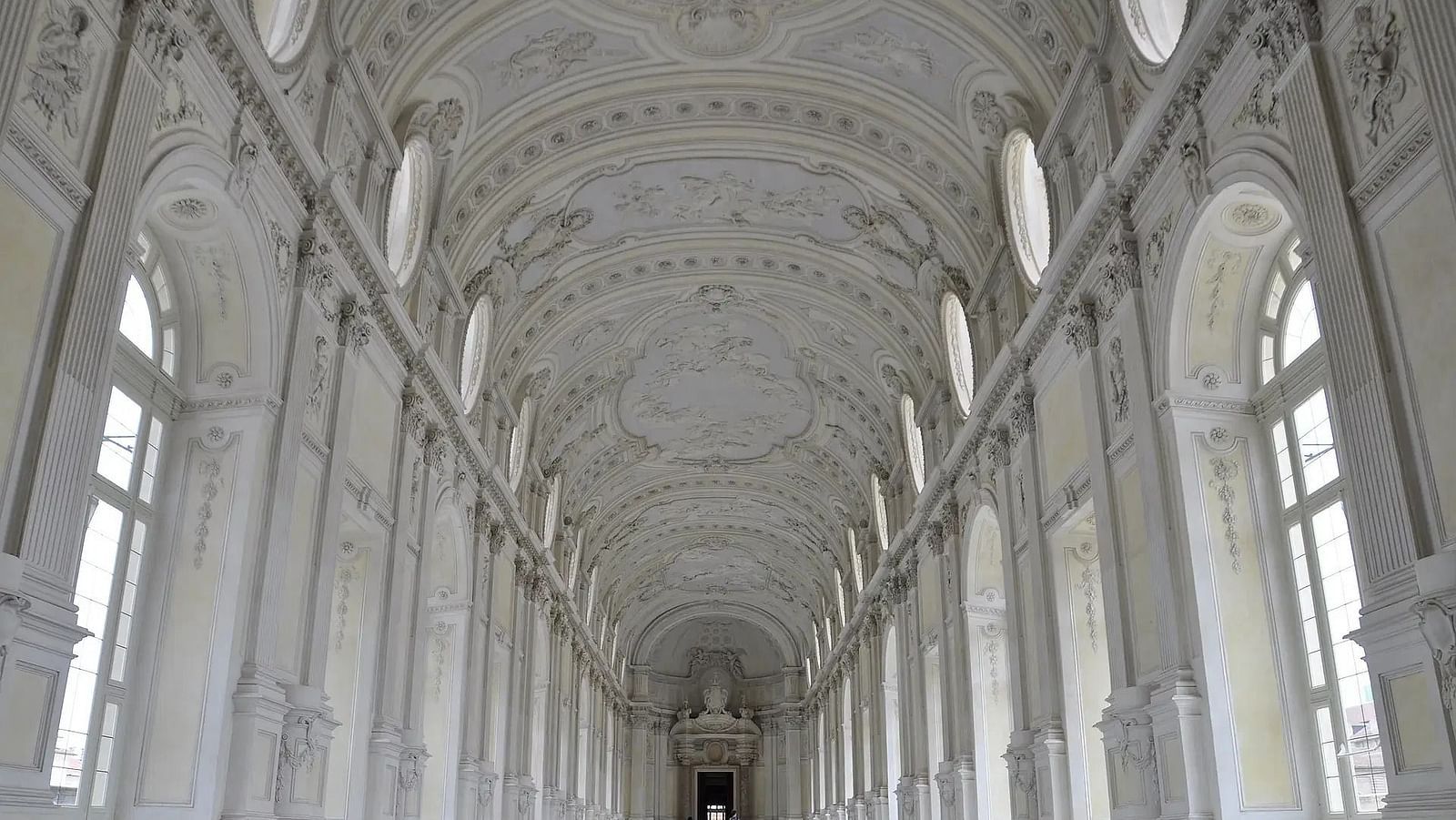 Arched ceiling of a grand hall, long and symmetrical, with a figure walking.