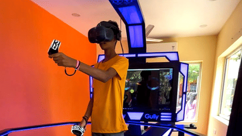 A person wearing a virtual reality headset and holding controllers while standing inside a futuristic VR gaming setup with blue lighting at Black Thunder, Coimbatore
