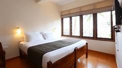 The deluxe room bedroom at Abad Serviced Villas, Kovalam with a double bed, bedside table, lamp, and large windows.