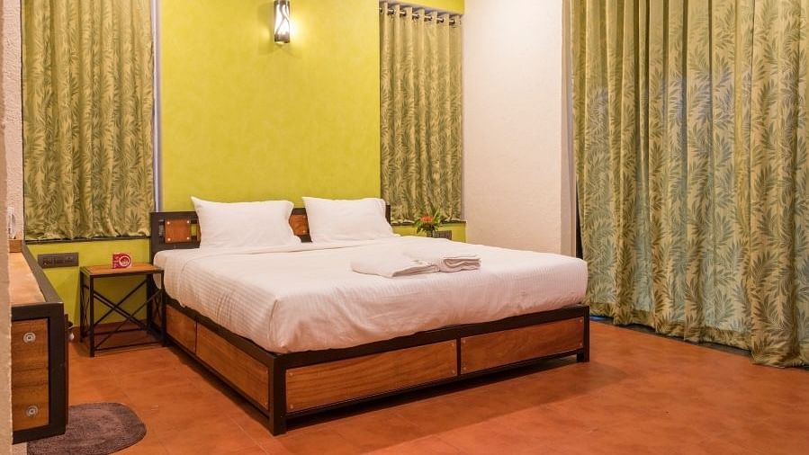 A bedroom with a wooden bed frame, white linens, lime green walls, matching curtains, and a dark wood side table.