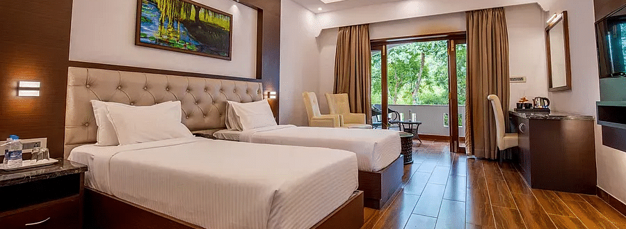 Deluxe Twin room with two single cot, bedside table, chair and a big glass windows at Avana Resort