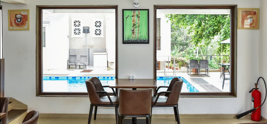 Dining space with wooden table and chairs near poolside windows, filled with natural light at La Vida Studio Inn.