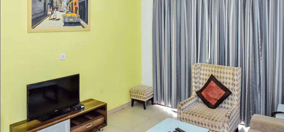 A spacious room with a television, armchair, and a small table at La Vida Studio Inn Goa.