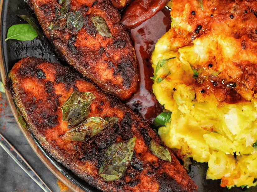 A vibrant Kerala-style meal features spiced fish, roasted vegetables, curry, and golden mashed potatoes served on a plate.