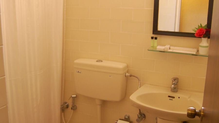 Bathroom of the Deluxe Suite Room at Green Pastures Kodaikanal featuring a clean layout with modern fixtures including a toilet, sink, mirror, and shower area.