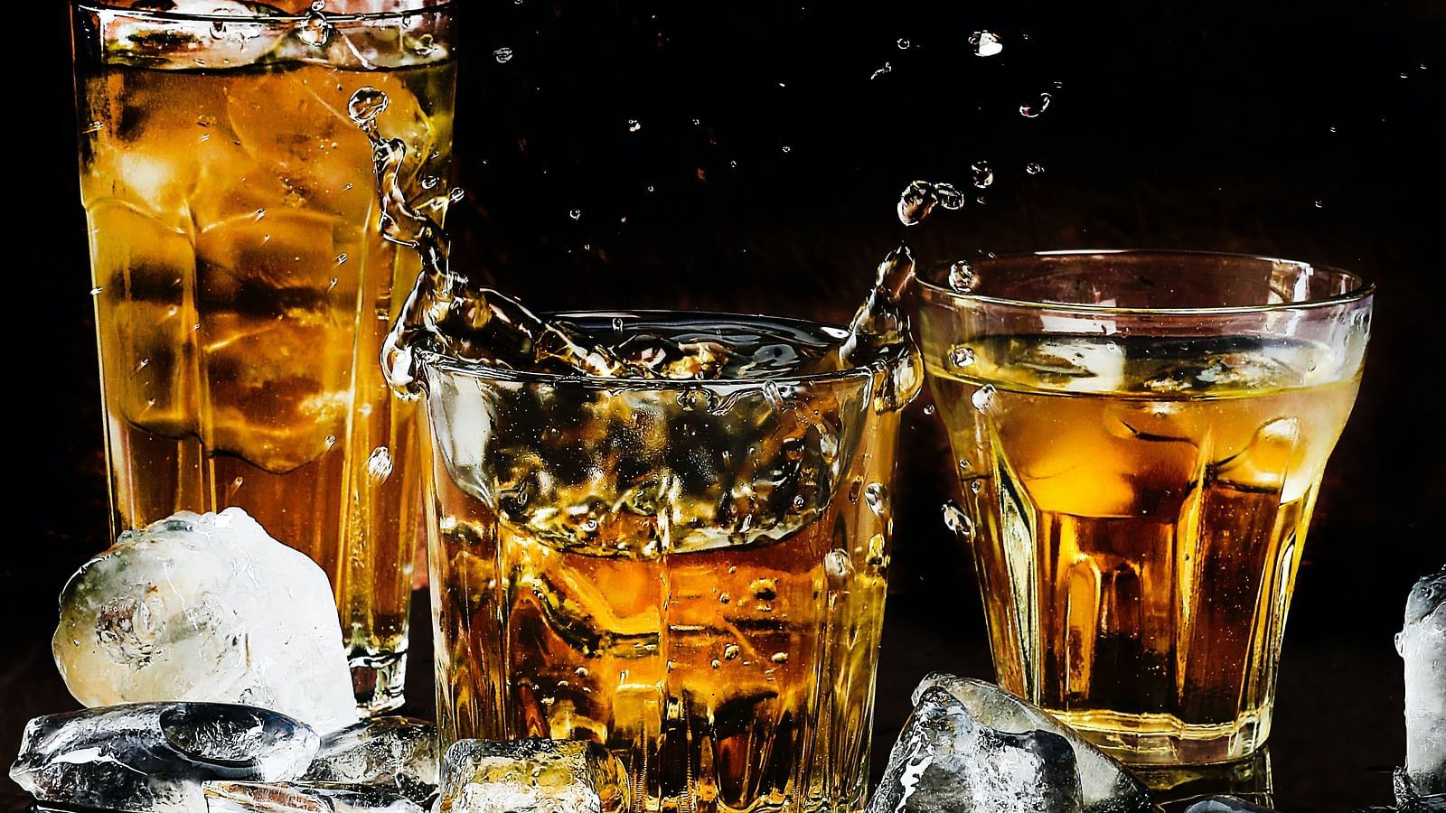 Three glasses of whiskey with ice cubes splashing out on a dark background