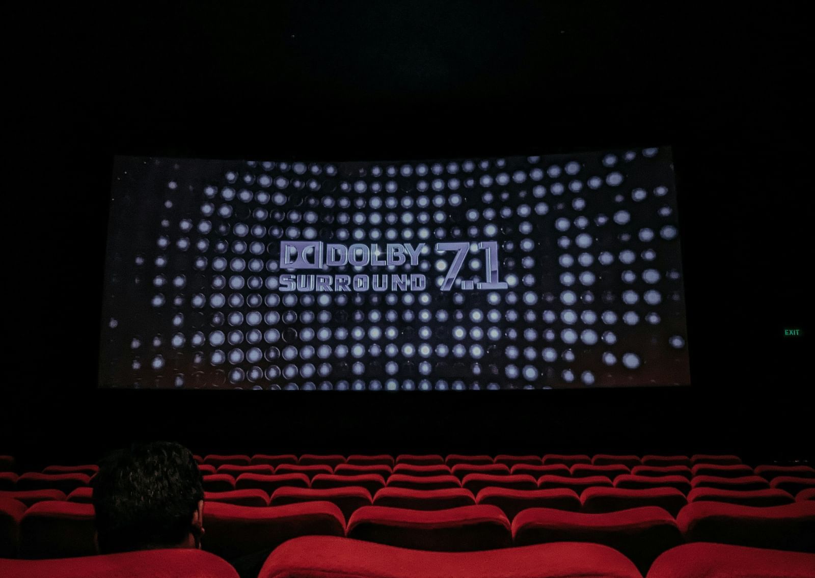A view from inside a theatre of a movie screening with red chairs in the foreground and a screen in the background.