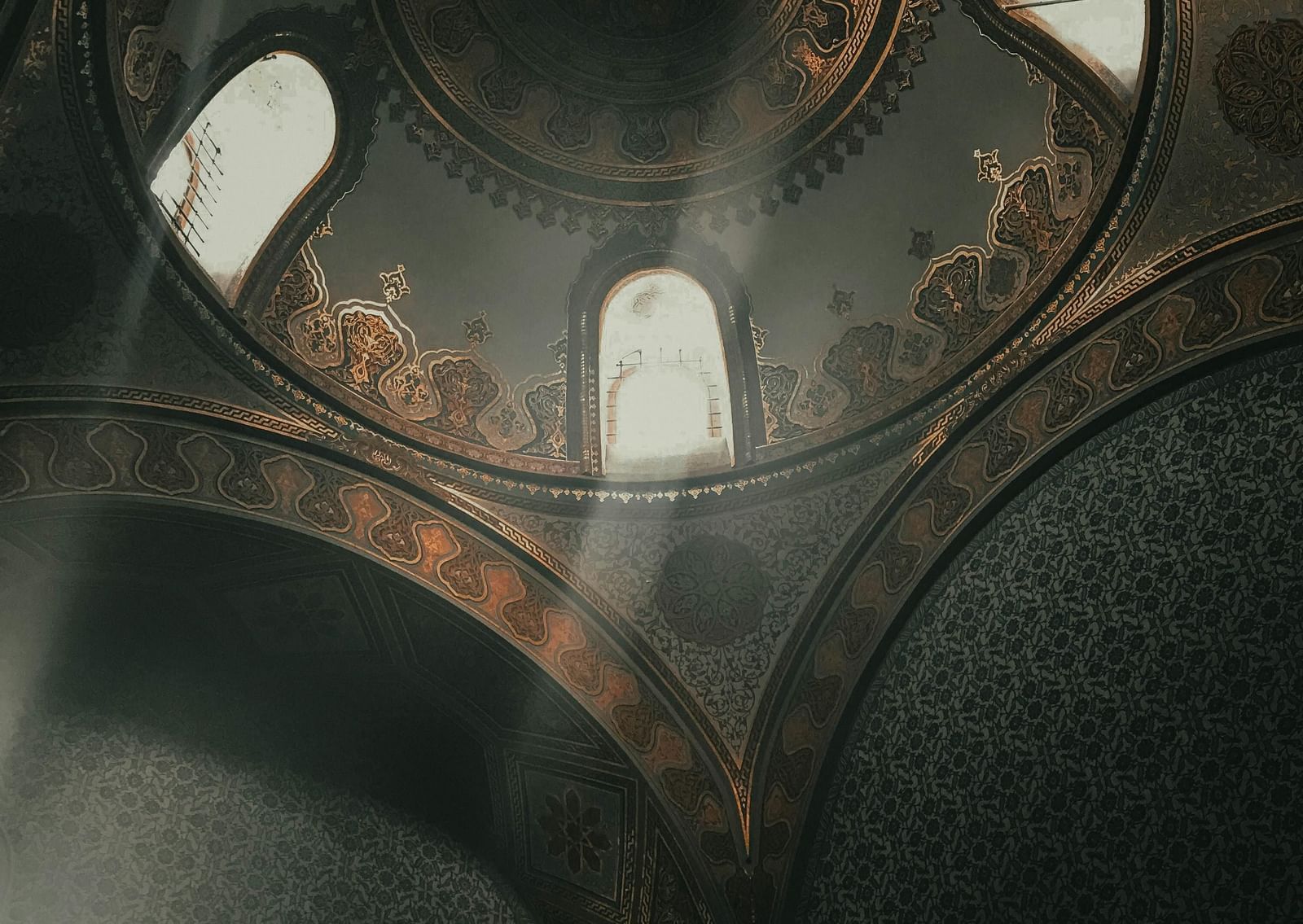 A unique interior shot looking up into the corner of a domed ceiling with arches and windows, showcasing complex stone and possibly mosaic patterns.