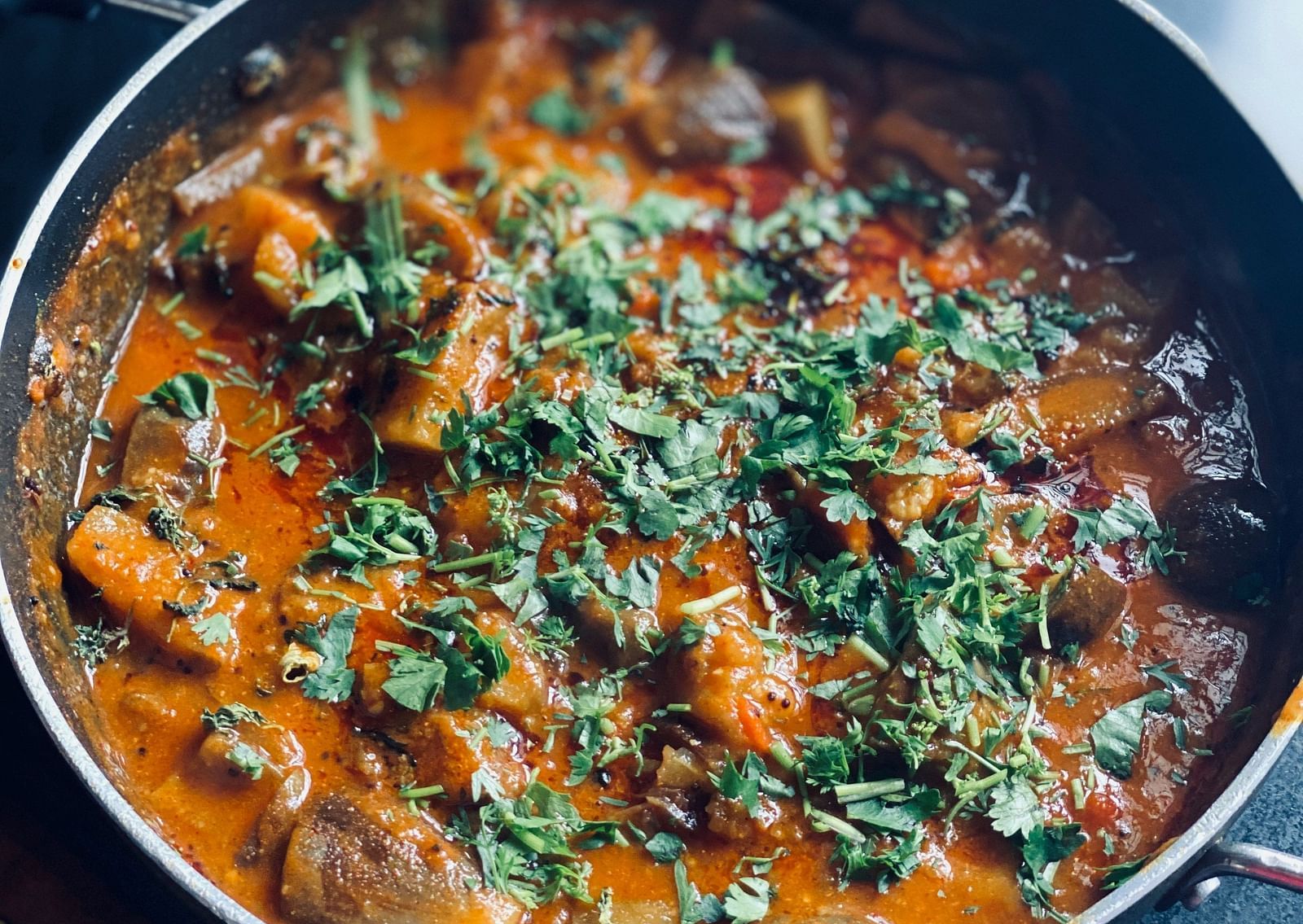 A close up shot of an Indian curry in a bowl with garnishing on top.