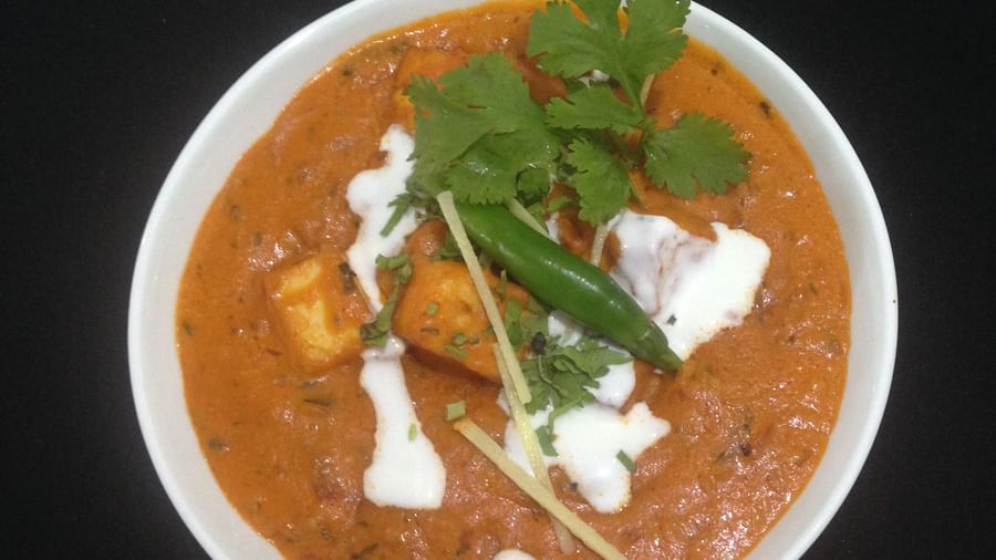A vibrant bowl of paneer butter masala garnished with a swirl of cream and cilantro | Daksh The Madhuvan Suites
