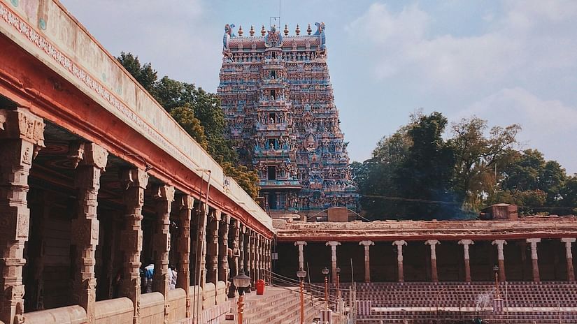 A temple with intricate architecture and colourful statues under a blue sky, beside a tank with steps