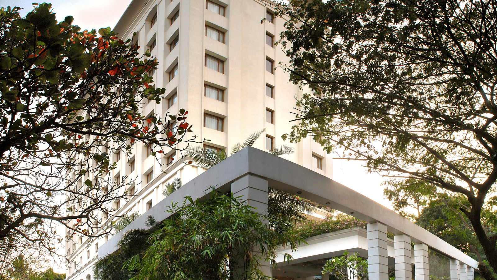 Facade view of The Raintree, St. Mary's Road - Hotel Near Chennai Trade Centre, surrounded by greenery under a vibrant sky