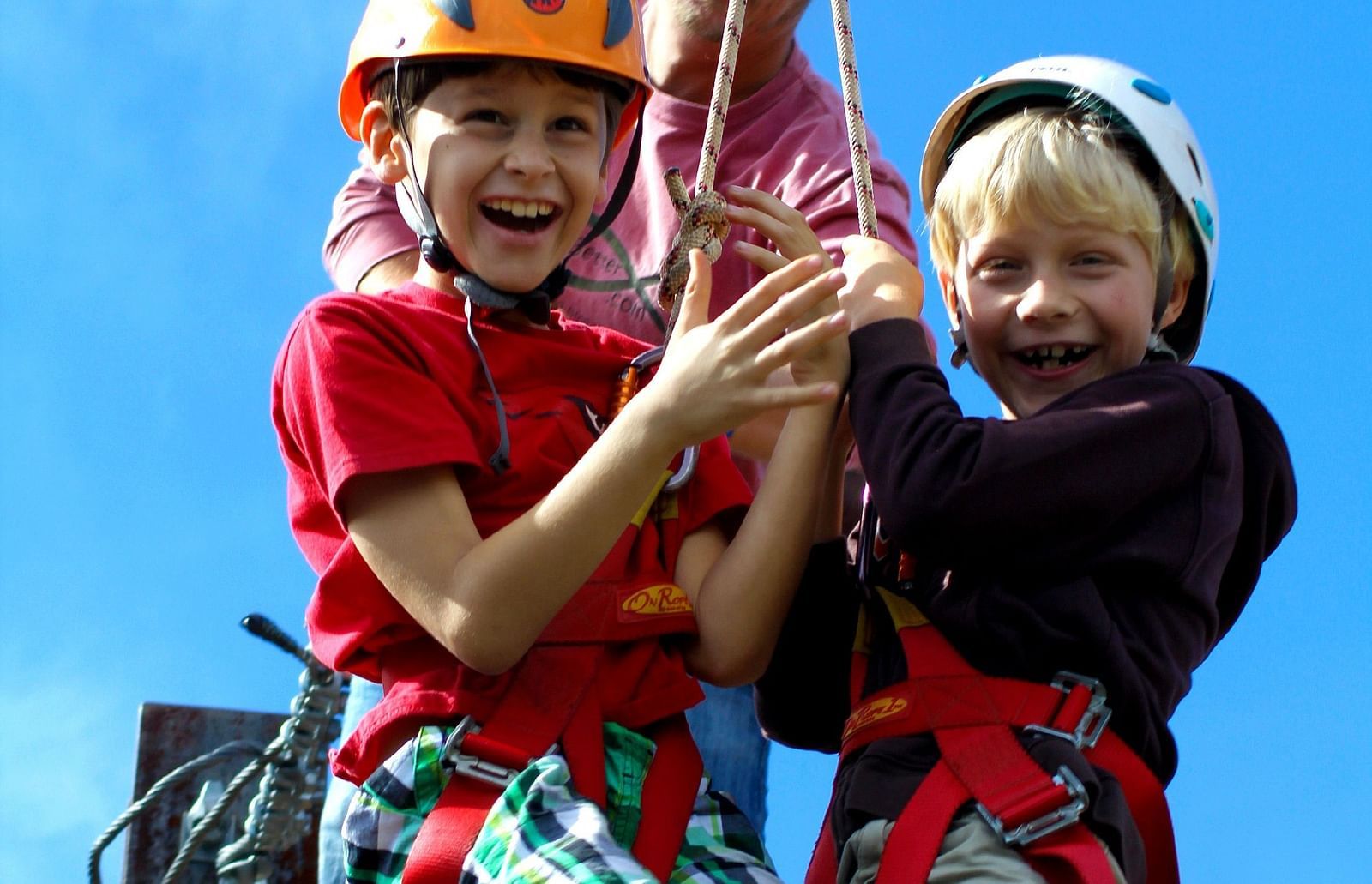 A close up shot of two kids laughing while standing on the ledge before zip-lining.