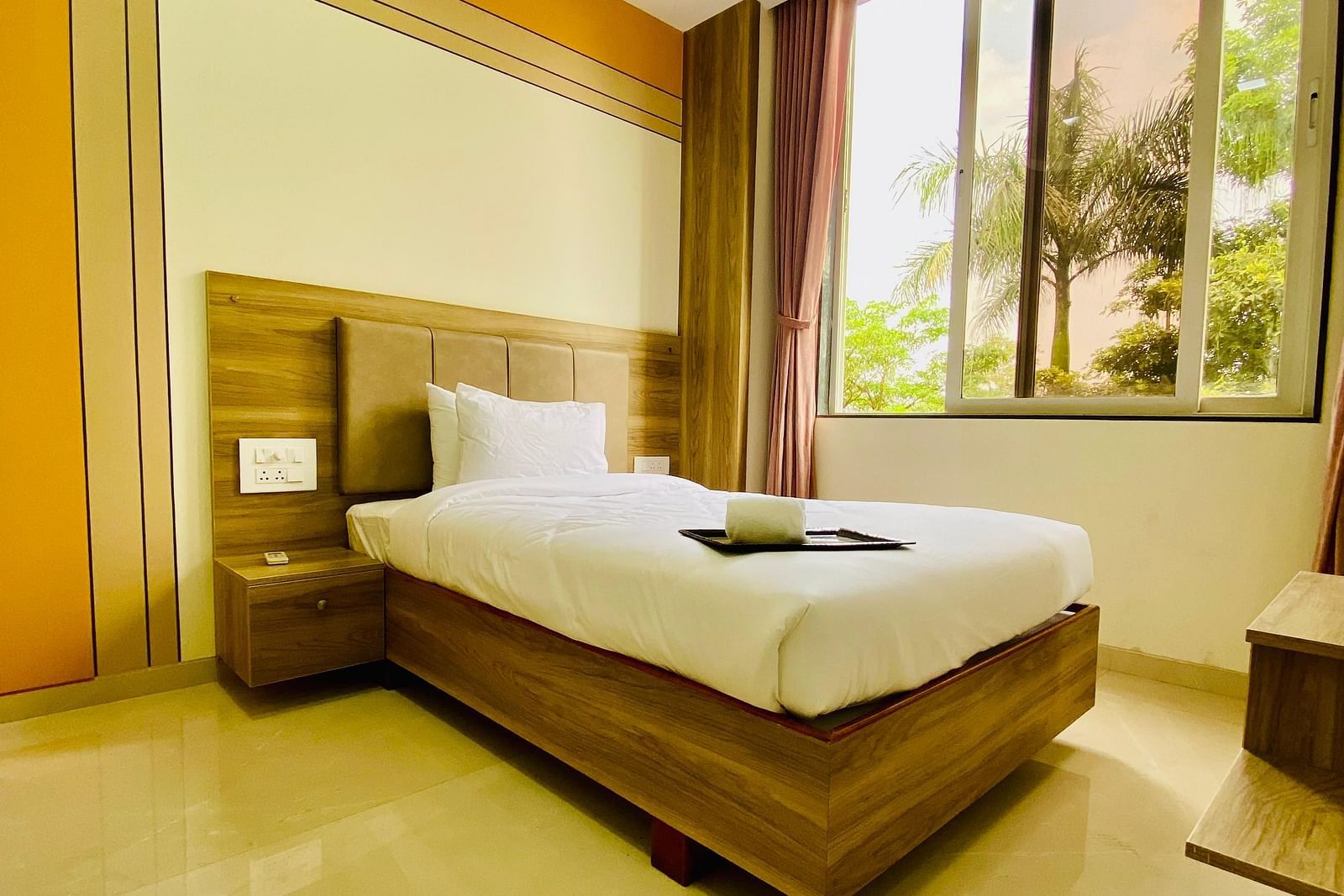 A bright hotel room featuring a neatly made bed, large windows, and a peaceful view of the outdoors.