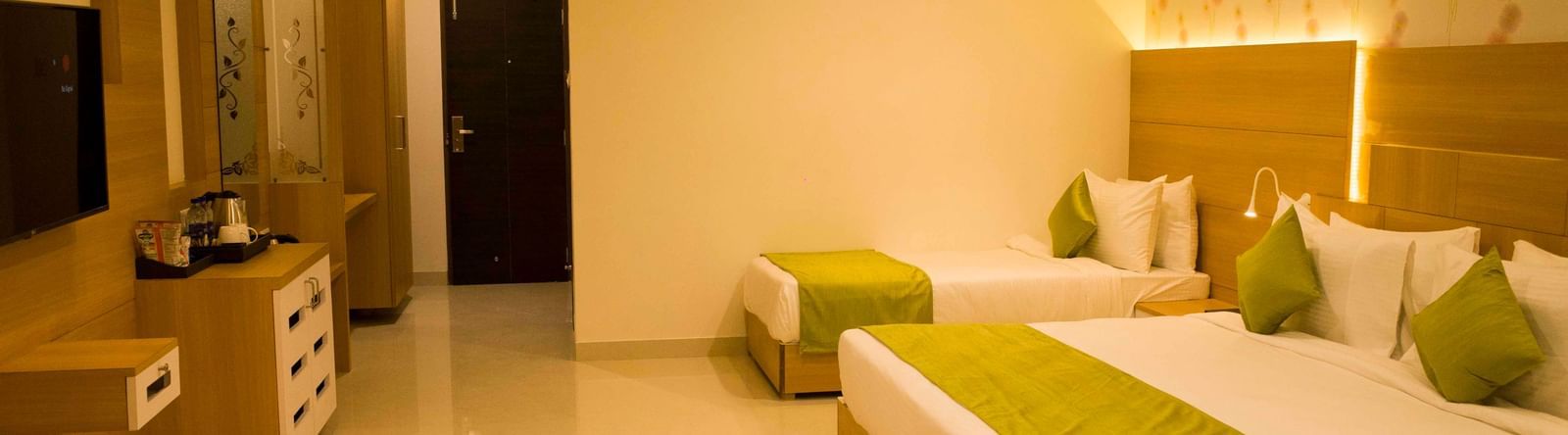 A hotel bedroom with warm lighting, a large bed, a single bed, with low headboards and a wall-mounted television | Daksh Pride Room | Daksh The Madhuvan Suites