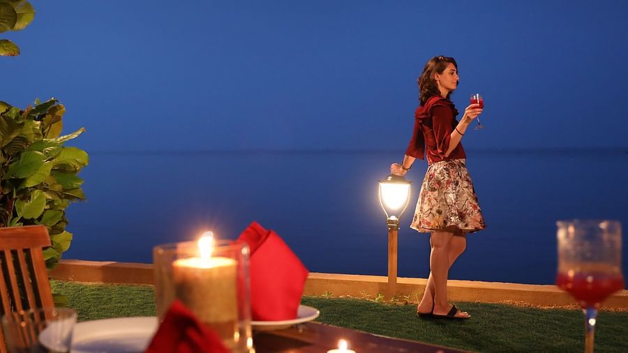 Romantic seaside dinner with candlelit table, gourmet food, and a woman gazing at the ocean under a deep blue evening sky at Uday Backwater Resort