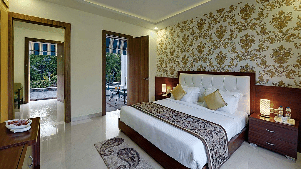 A spacious bedroom at Clarks Safari, Ranthambore, featuring a comfortable bed, a balcony overlooking the surrounding greenery, and elegant decor.