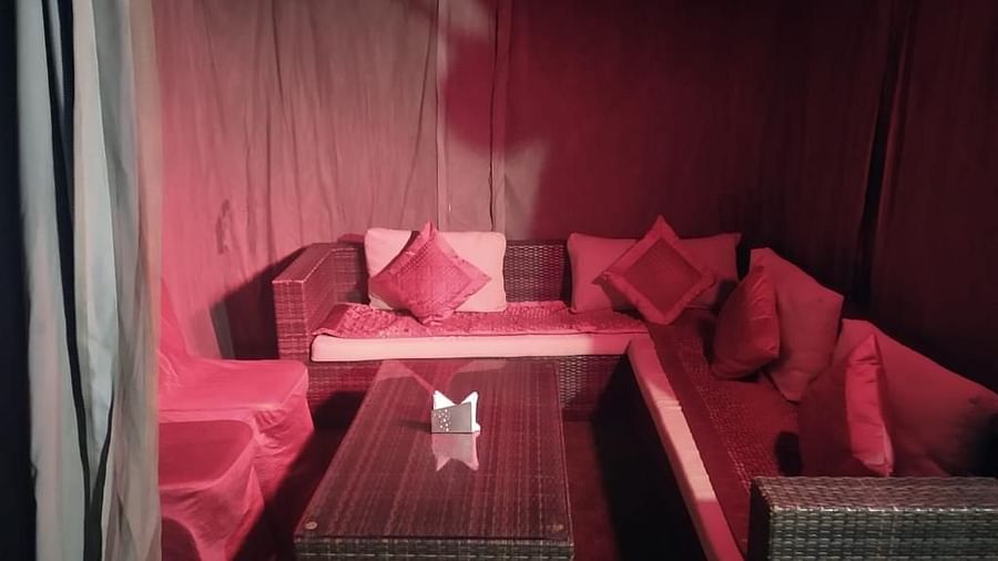 A cushioned sofa with a table in the middle and curtains to the side at Hotel Uday Palace.